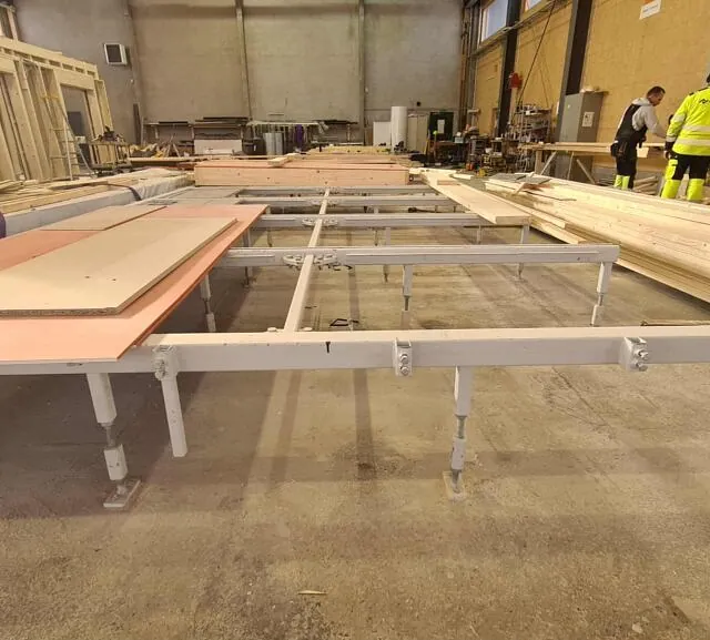Produksjonslokale med arbeidsbord og materialer for bygging av veggelementer innendørs.