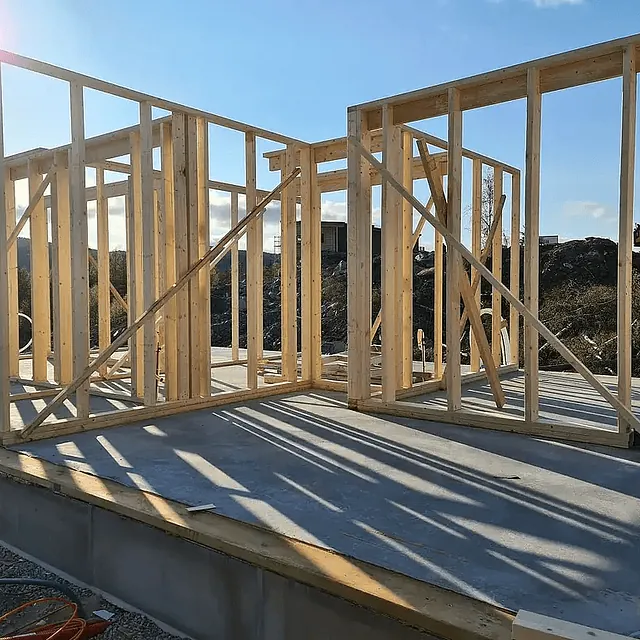 Reisverk i tre på betongplate under oppføring av bolig med tydelig konstruksjon i dagslys.