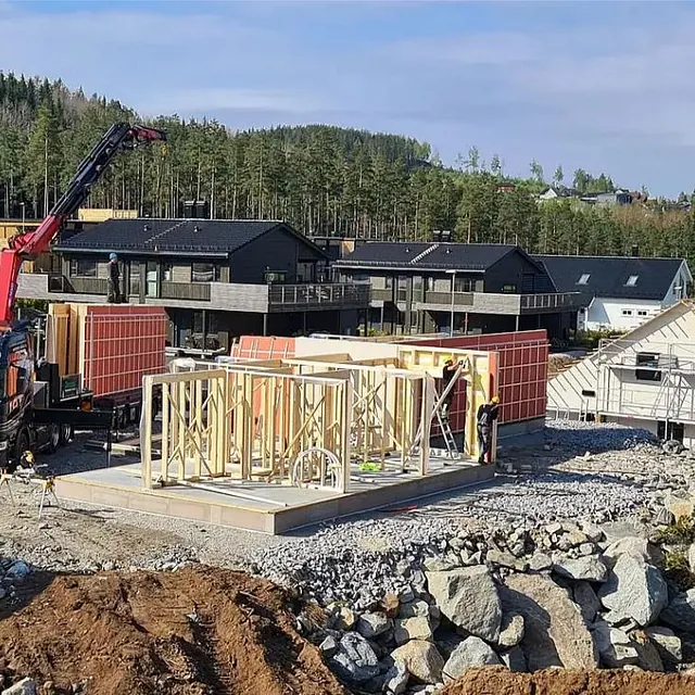 Bolig under bygging med kranbil, reisverk og byggeplass i etablert boligområde.