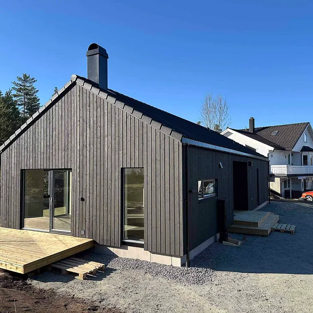 Moderne enebolig med trekledning, terrasse og store vinduer i rolige og naturnære omgivelser.